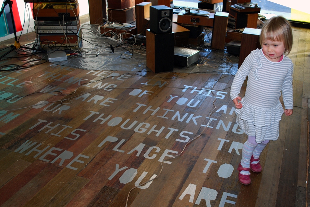 WE ARE HERE, IN THIS PLACE, THINKING OF YOU, AND WHILE WE ARE THINKING OF YOU, OUR THOUGHTS TRAVEL FROM THIS PLACE TO THE PLACE WHERE YOU ARE NOW mark booth THE SOUND OF THE WORD SPEED / THE SPEED OF THE WORD SOUND Floor text hand-cut adhesive silver vinyl and loudspeakers