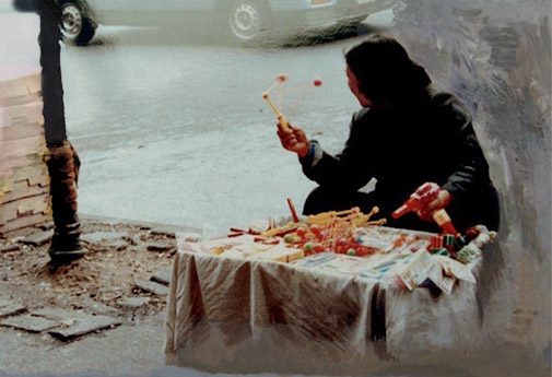 A woman peddler (spinning a Tibetan-prayer-wheel-like toy in one hand, and a plastic gun in the other, in Canal Street traffic.)